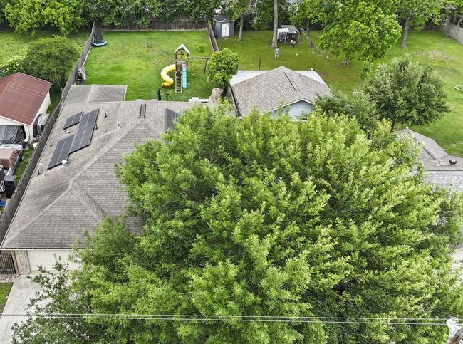 This aerial photo showcases a residential property with a spacious backyard, mature trees, and a playset, indicating a family-friendly environment. The house features solar panels, suggesting energy efficiency. | Image 8