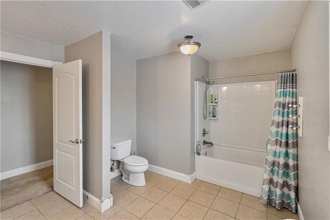 Bathroom with shower / tub combo with curtain, toilet, tile patterned flooring, and a textured ceiling | Image 34