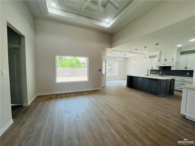 Kitchen with dark hardwood / wood-style flooring, a raised ceiling, a center island with sink, and white cabinets | Image 3