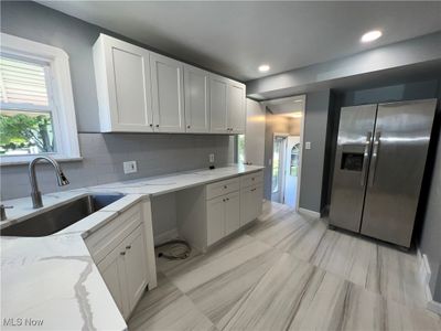 Kitchen with white cabinets, light stone counters, sink, and stainless steel fridge | Image 3