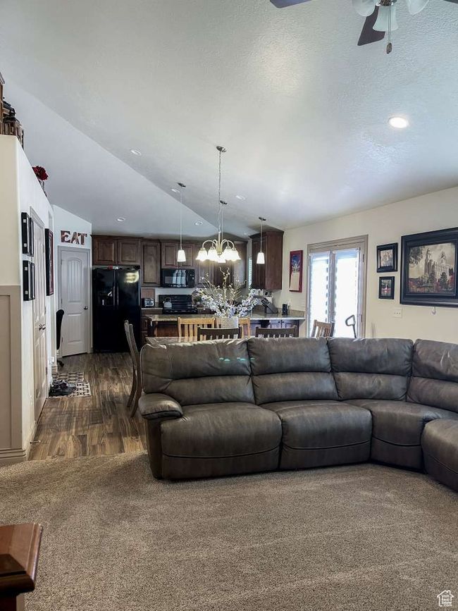 Living area featuring ceiling fan, a chandelier, vaulted ceiling, dark colored carpet, and dark wood-style flooring | Image 14