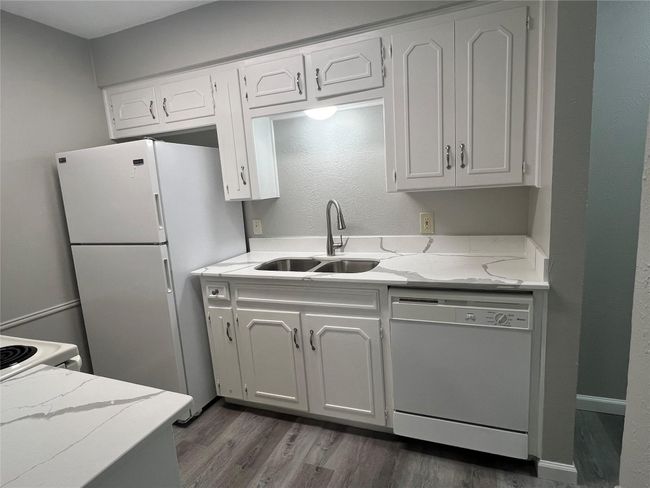 Kitchen featuring white appliances, light stone counters, dark wood-style flooring, and white cabinets | Image 6