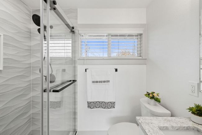The owner's suite bathroom has a large vanity with a quartz countertop, elegant modern tile shower with a large stone niche, hexagon tile flooring, large framed mirror and black fixtures. | Image 20