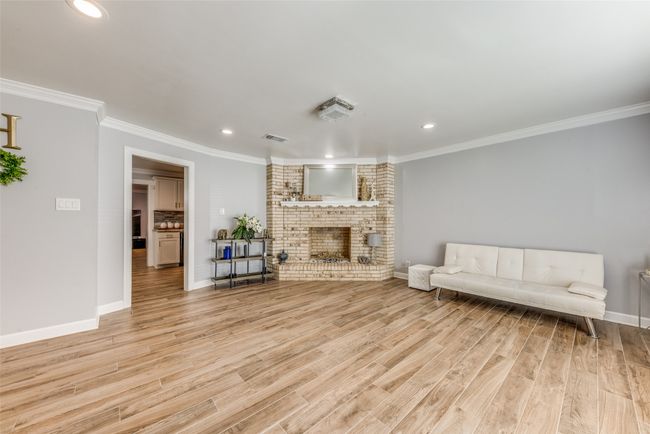 Living area featuring light wood-style flooring, crown molding, a fireplace, and recessed lighting | Image 6