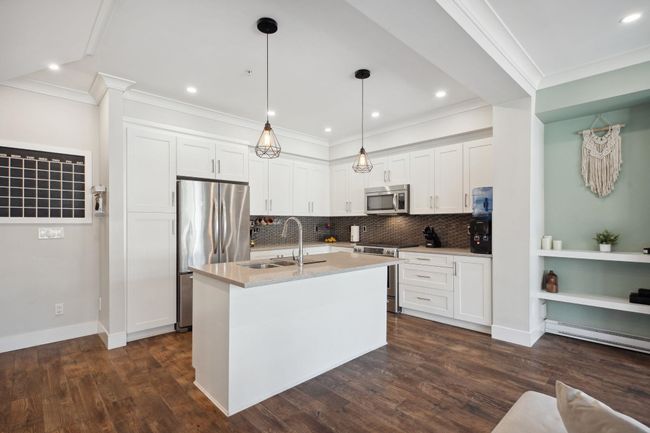 Kitchen with white cabinets, a sink, ornamental molding, dark wood-style flooring, and appliances with stainless steel finishes | Image 11