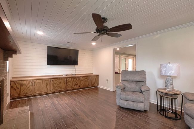 Living area featuring dark wood-type flooring, ceiling fan, wooden ceiling, wood walls, and ornamental molding | Image 9