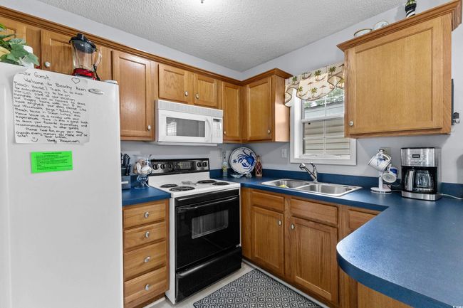 Kitchen with white appliances, a sink, dark countertops, a textured ceiling, and brown cabinets | Image 12