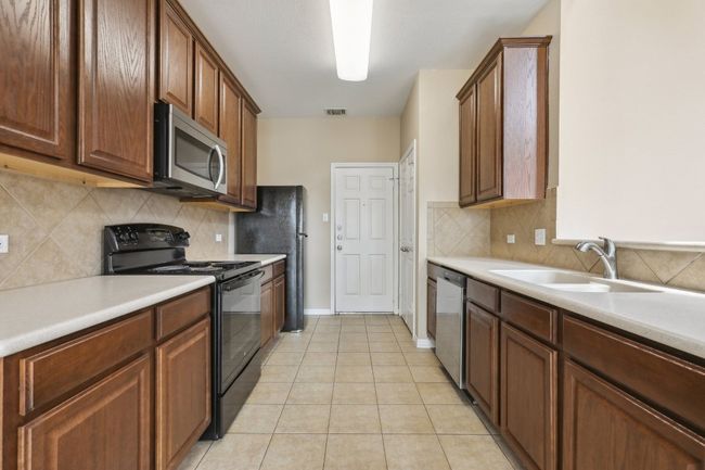 Kitchen featuring tasteful backsplash, light tile patterned floors, light countertops, black appliances, and a sink | Image 13