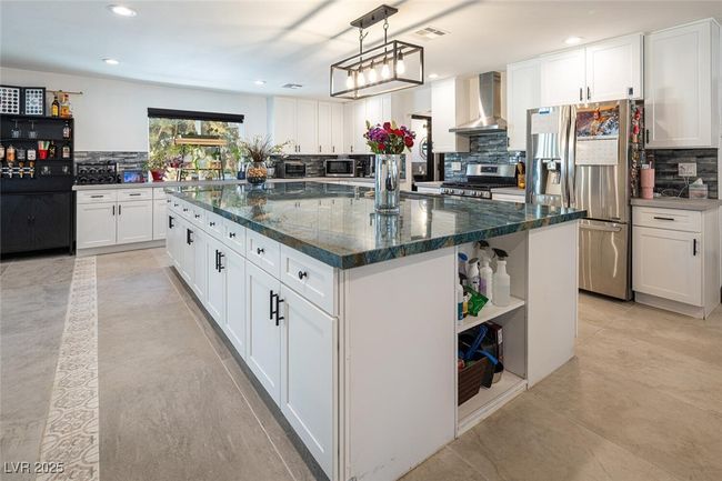 Kitchen with open shelves, stainless steel appliances, white cabinets, wall chimney range hood, and a center island | Image 13