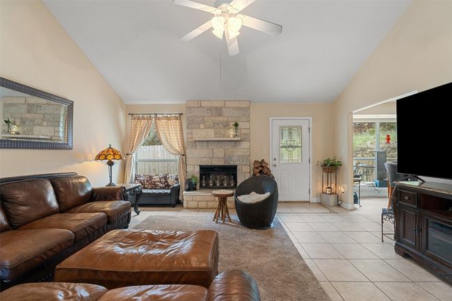 Living room featuring light tile patterned floors, ceiling fan, high vaulted ceiling, a stone fireplace, and baseboards | Image 5