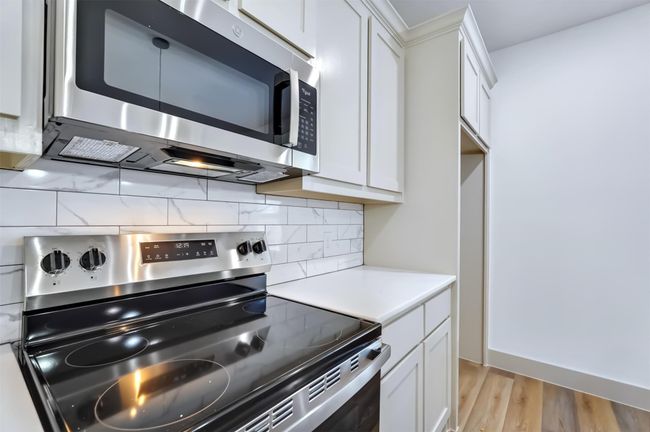 Kitchen featuring tasteful backsplash, light countertops, white cabinets, and stainless steel appliances | Image 6