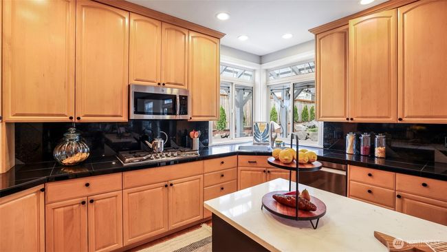 The kitchen showcases sleek black granite tile countertops, warm wood cabinetry, a spacious open layout, a double sink, a large window above the sink that brings in natural light, and a stylish backsplash | Image 21