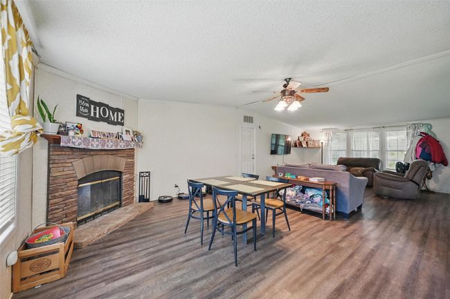 Dining area featuring wood finished floors, a textured ceiling, a ceiling fan, a fireplace, and lofted ceiling | Image 5