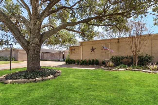 This front yard features a lush green lawn and a striking mature tree that provides ample shade. A well-defined landscaping bed surrounds the base of the tree, complementing the neatly arranged shrubbery along the home's brick exterior. The spacious driveway offers easy access to the garage and entryway. | Image 5