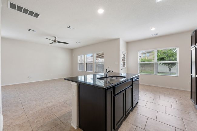 Kitchen featuring a sink, stainless steel dishwasher, light tile patterned floors, dark stone counters, and ceiling fan | Image 9