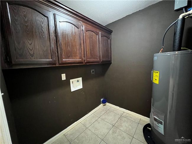 Washroom with water heater, tile patterned floors, a textured ceiling, cabinet space, and baseboards | Image 11