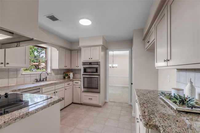 This kitchen features granite countertops, ample cabinetry, stainless steel appliances, and tile flooring. A window above the sink offers natural light, and there's a clear view into an adjacent dining area. | Image 18