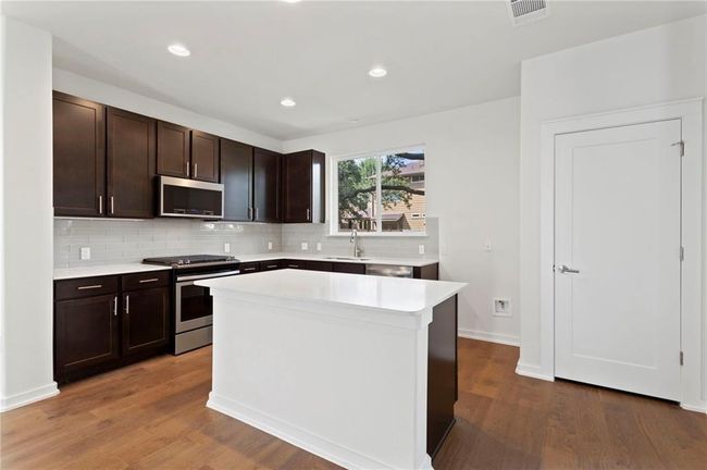 Kitchen with stainless steel appliances, light countertops, dark brown cabinets, tasteful backsplash, and wood finished floors | Image 9