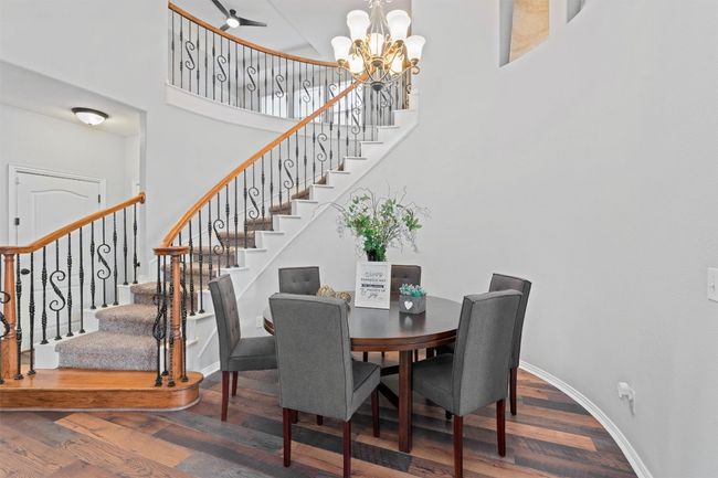 Dining space featuring a towering ceiling, wood finished floors, a chandelier, and stairs | Image 10
