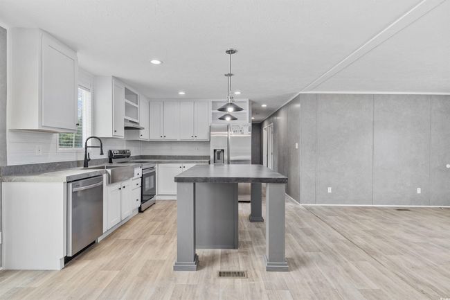 Kitchen with stainless steel appliances, open shelves, white cabinets, dark countertops, and light wood-style floors | Image 15