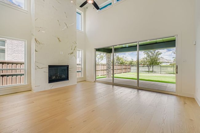 Unfurnished living room with a ceiling fan, light wood finished floors, a high ceiling, and a fireplace | Image 4