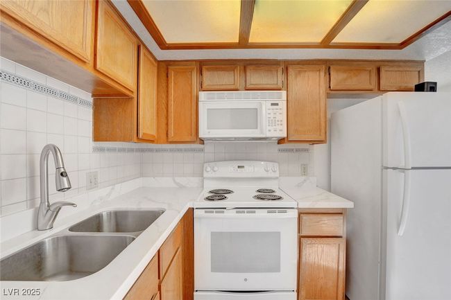 Kitchen with tasteful backsplash, a sink, white appliances, and light stone countertops | Image 12