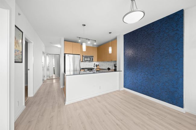 Kitchen featuring stainless steel appliances, dark countertops, light wood-type flooring, wallpapered walls, and a peninsula | Image 12
