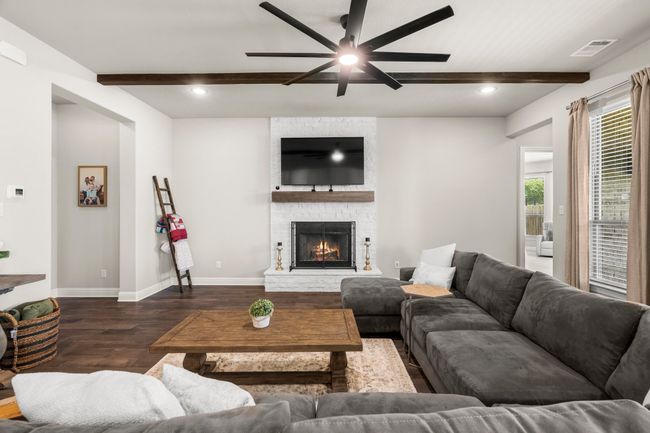Living area with ceiling fan, dark wood-style flooring, beamed ceiling, a stone fireplace, and recessed lighting | Image 5