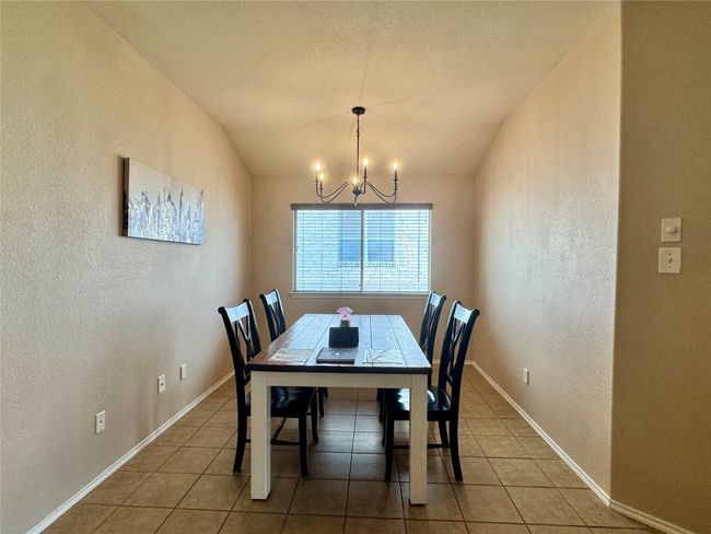 Dining area with a textured wall, a chandelier, tile patterned floors, and lofted ceiling | Image 17