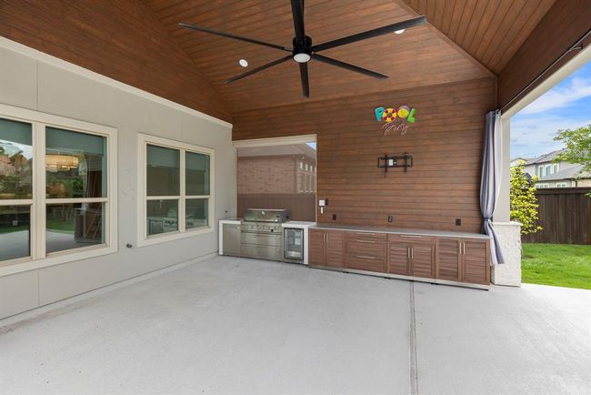 This expansive outdoor kitchen is equipped with a built-in grill, beverage fridge, TV connections and ample cabinetry beneath a soaring wood-paneled ceiling—perfect for poolside entertaining. | Image 44