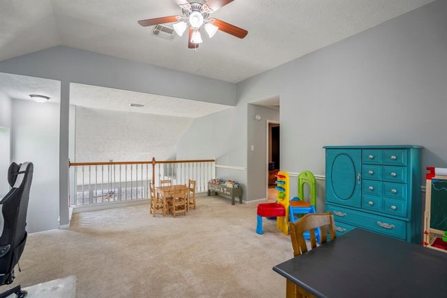 From this angle, we get a broader view of the spacious game room, showcasing the vaulted ceilings and natural light flooding in from the windows. The open feel is enhanced by the view towards the staircase, balcony railing, and the hallway leading to the media room, emphasizing the expansive layout of this flexible space. | Image 25