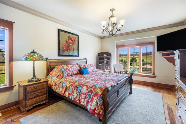 Bedroom with a chandelier, & bow window ornamental molding, wood finished floors, and baseboards | Image 27