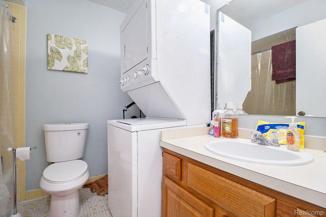 Full bath featuring stacked washer and clothes dryer, vanity, a shower with curtain, and tile patterned flooring | Image 15
