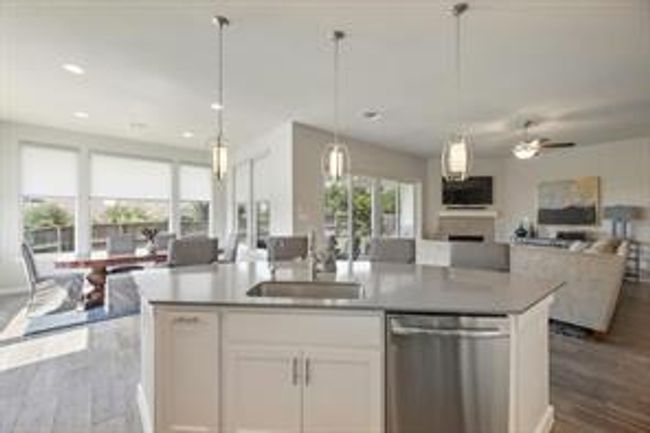 Kitchen with open floor plan, stainless steel dishwasher, dark wood-style flooring, white cabinetry, and an island with sink | Image 10