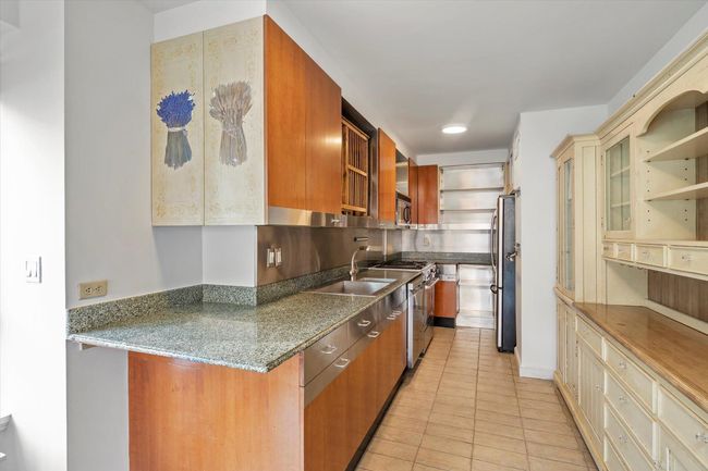 Kitchen featuring stainless steel appliances, open shelves, light tile patterned flooring, a sink, and dark stone countertops | Image 9