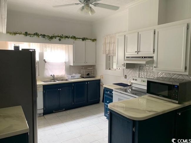 Kitchen with white appliances, blue cabinets, a sink, under cabinet range hood, and a ceiling fan | Image 6