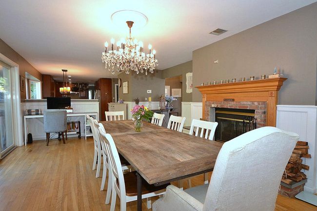 Dining room with a chandelier, a wainscoted wall, light wood finished floors, visible vents, and a fireplace | Image 6