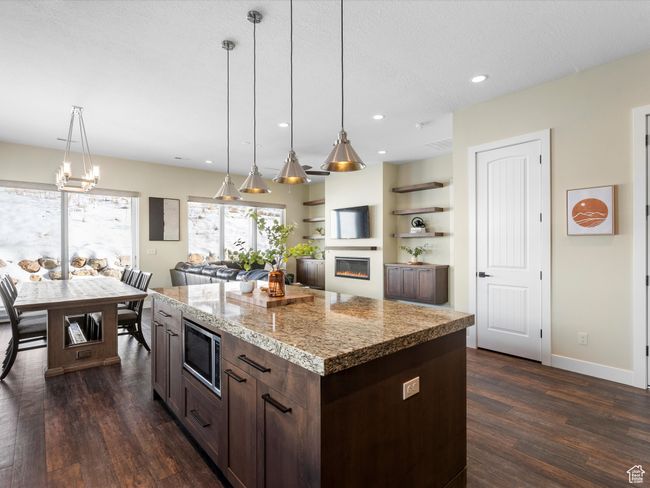 Kitchen featuring stainless steel microwave, dark wood-style flooring, dark brown cabinets, a glass covered fireplace, and decorative light fixtures | Image 5