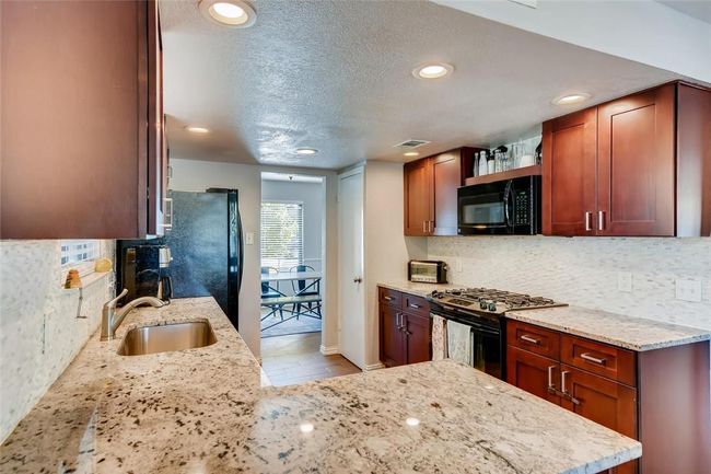 Kitchen featuring black appliances, a sink, light stone countertops, decorative backsplash, and recessed lighting | Image 11
