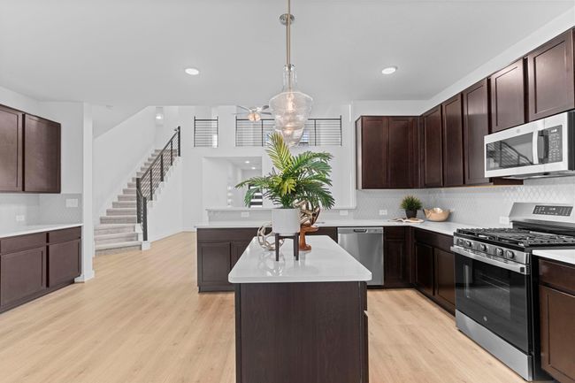 Expansive view of the kitchen and breakfast area featuring a large center island, modern pendant lighting, and open sightlines to the staircase and family room—designed for everyday comfort and entertaining. **Image Representative of Plan Only and May Vary as Built**. | Image 15