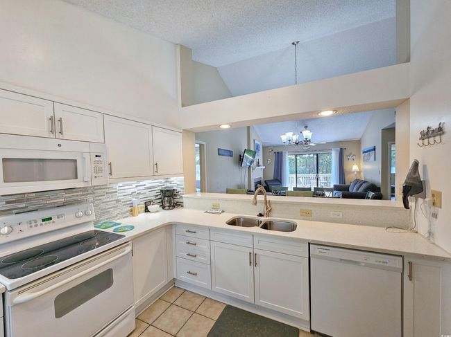 Kitchen featuring white appliances, a sink, a chandelier, vaulted ceiling, and light tile patterned floors | Image 14