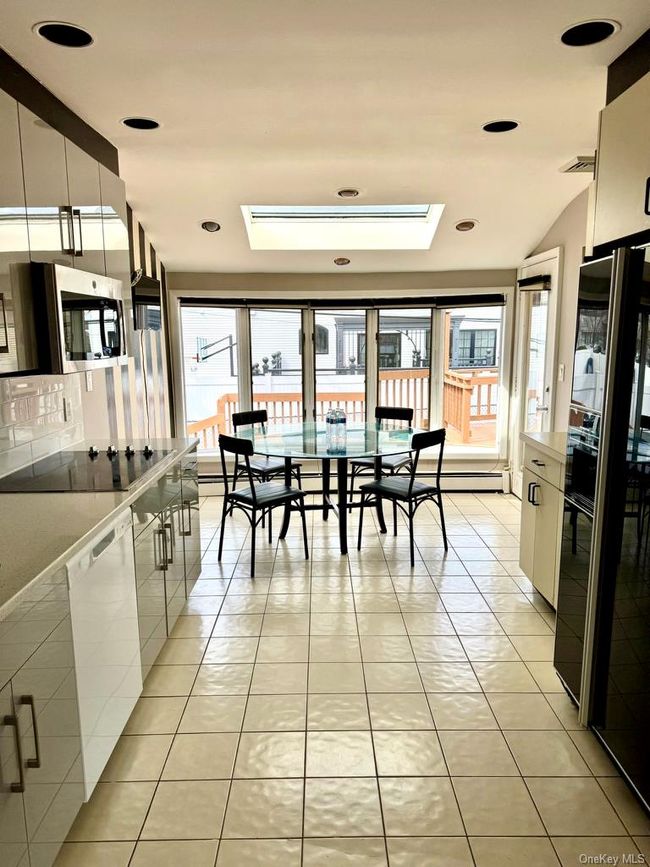 Kitchen featuring modern cabinets, black appliances, a skylight, and light tile patterned floors | Image 6