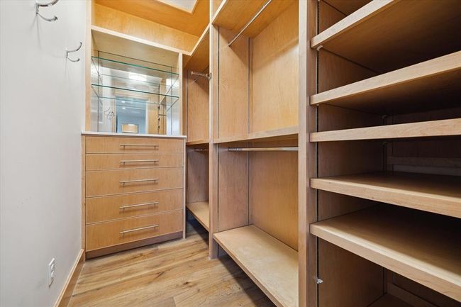 The second of two spacious primary closets, outfitted with custom cabinetry, adjustable open shelving, dual hanging areas, and sleek built-in drawers. A well-appointed space offering tailored storage and everyday convenience. | Image 20