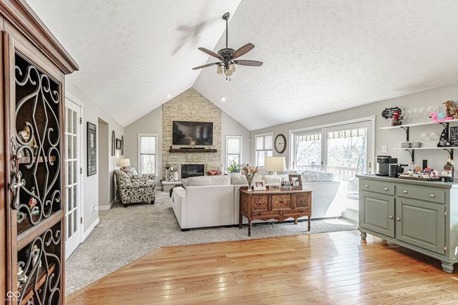 living room with vaulted ceiling, a ceiling fan, a textured ceiling, light wood finished floors, and a fireplace | Image 5