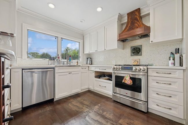 Kitchen with stainless steel appliances, custom range hood, a sink, white cabinets, and ornamental molding | Image 12