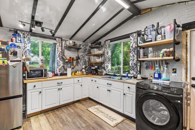 Kitchen featuring appliances with stainless steel finishes, washer / dryer, open shelves, a sink, and light wood-type flooring | Image 10
