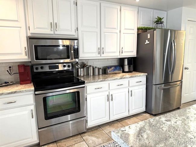 Kitchen featuring appliances with stainless steel finishes, decorative backsplash, white cabinets, and light tile patterned floors | Image 13