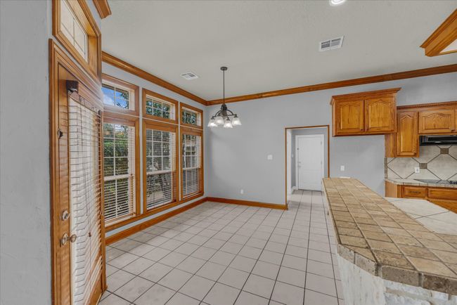 Kitchen featuring under cabinet range hood, decorative backsplash, crown molding, a chandelier, and light tile patterned floors | Image 10