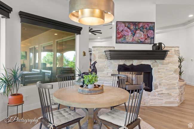 Dining room with ceiling fan, wood finished floors, a stone fireplace, ornamental molding, and baseboards | Image 43