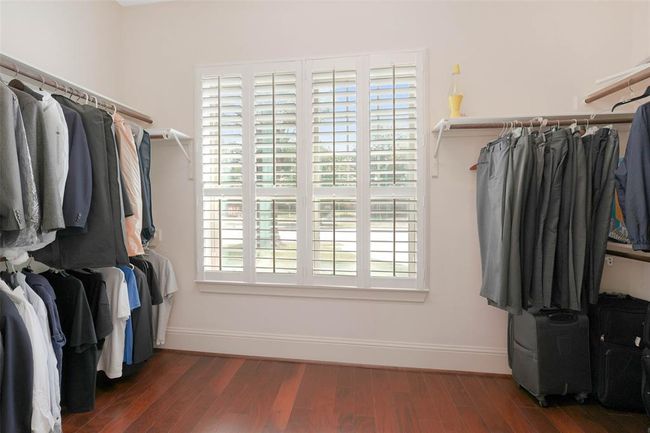 Spacious walk-in closet with hardwood flooring, built-in double hanging rods, and natural light from large plantation-shuttered windows. Offers ample storage and organization potential. | Image 30